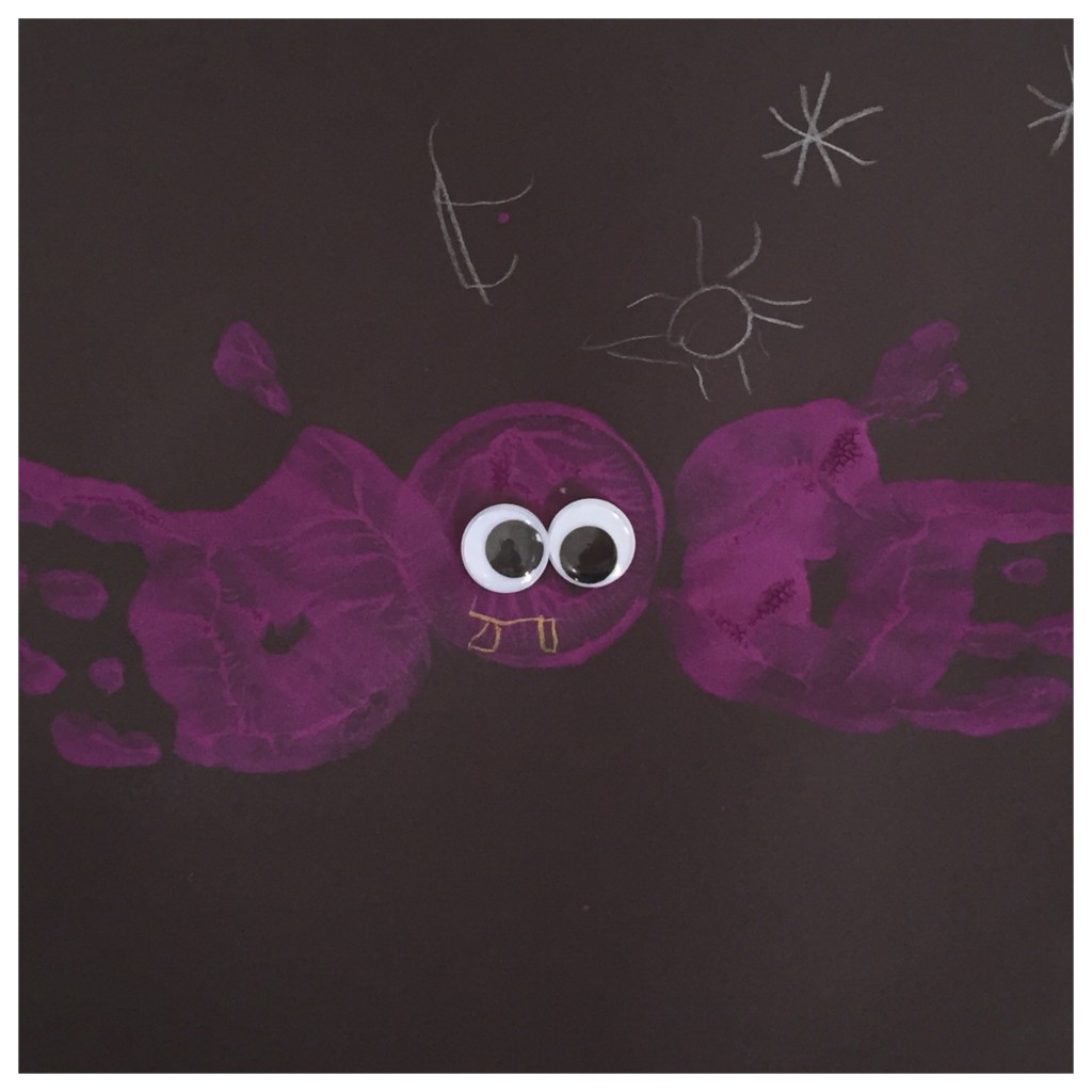 Purple handprint bat on black construction paper with googly eyes. 