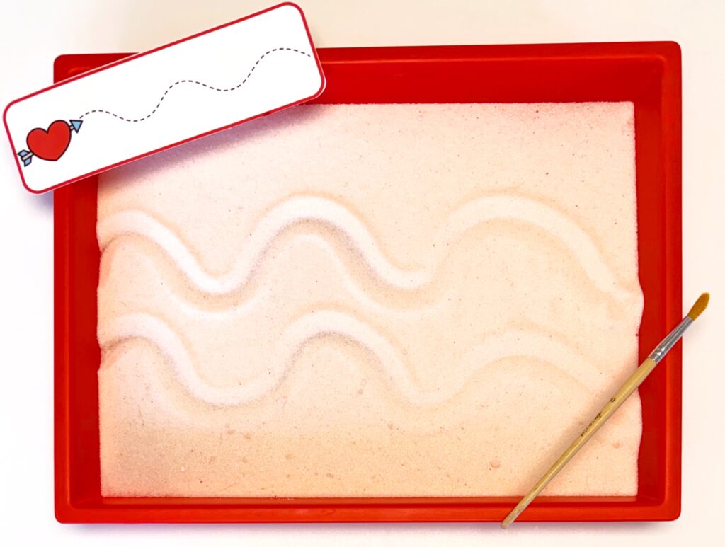 Prewriting Valentine's Day Activity using a salt tray with pink salt, curvy line